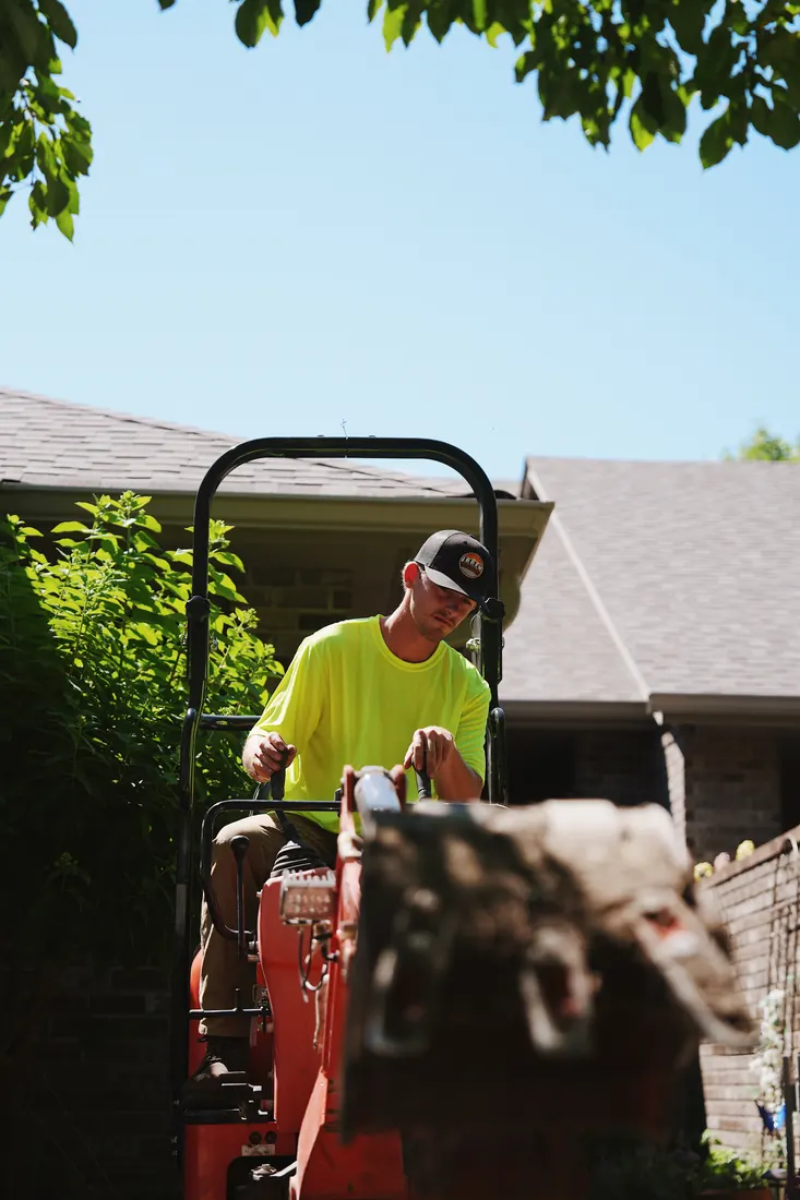 Lofton crew member running the mini excavator alongside a house