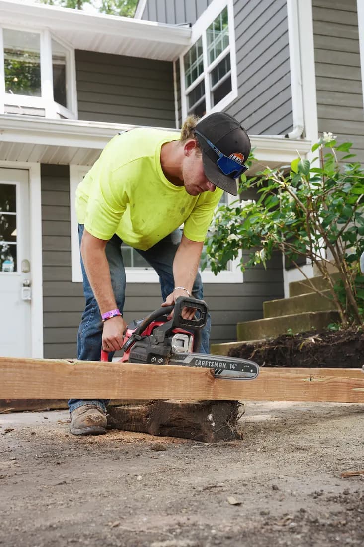 Crew member cutting a landscape timber to length with a chainsaw